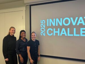 The winners of the 2025 Innovation Challenge standing next to the projection screen with the event's logo on it