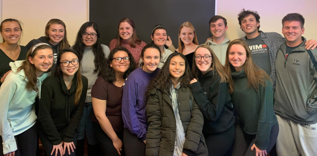 Group of college students posing for photo in front of wall