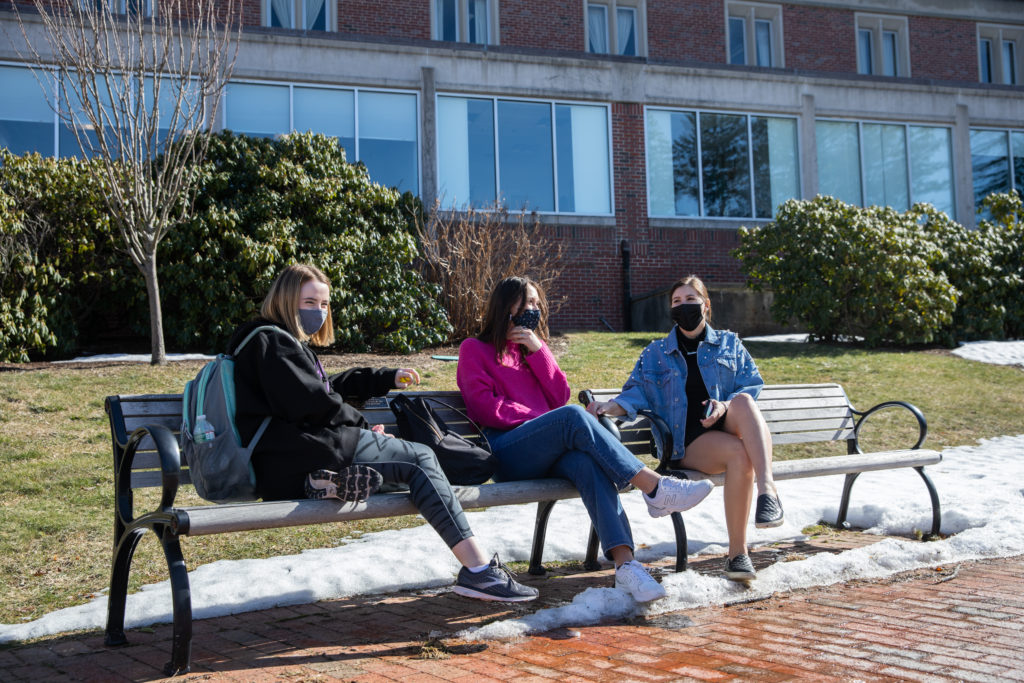 Three students sit on a bench