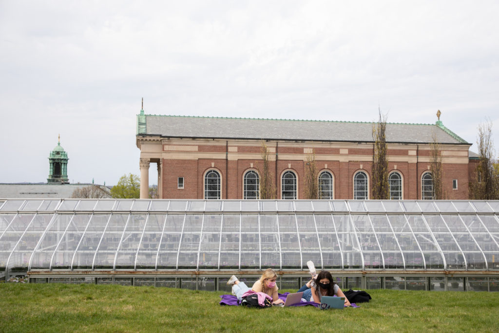 Two female students laying in front of a greenhouse